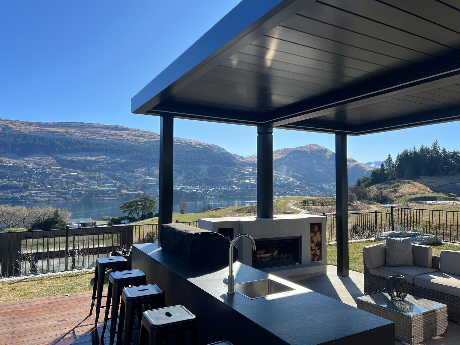 Black louvre roof over an outdoor kitchen and fireplace with Lake Wakatipu views in Queenstown