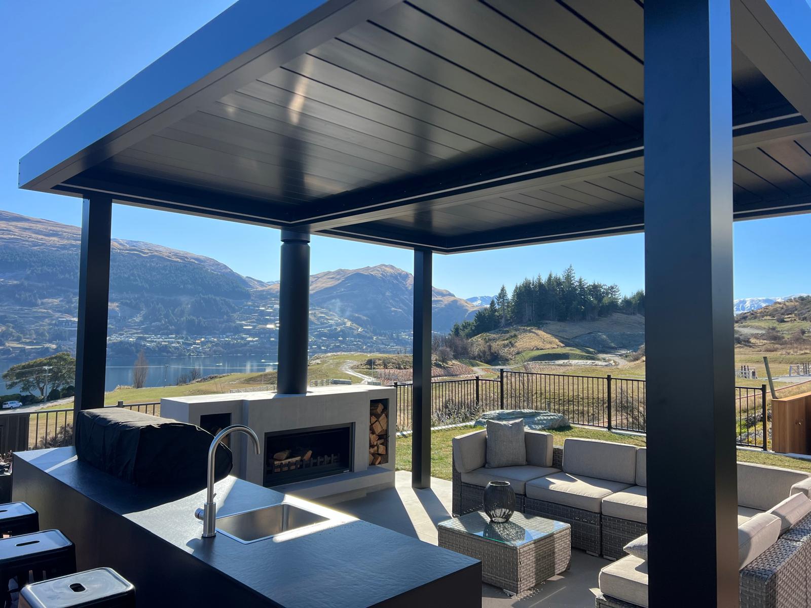 Closed black louvre roof over an outdoor lounge, kitchen and fireplace in Queenstown