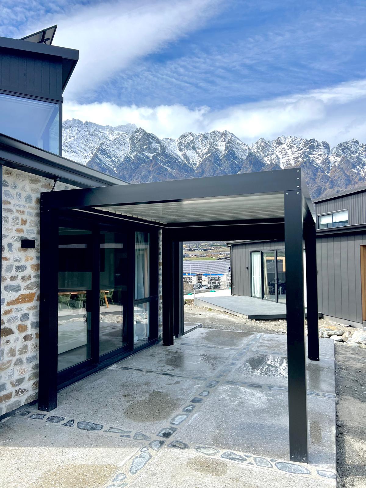 Black louvre roof over a stone-clad entry with The Remarkables behind in Queenstown