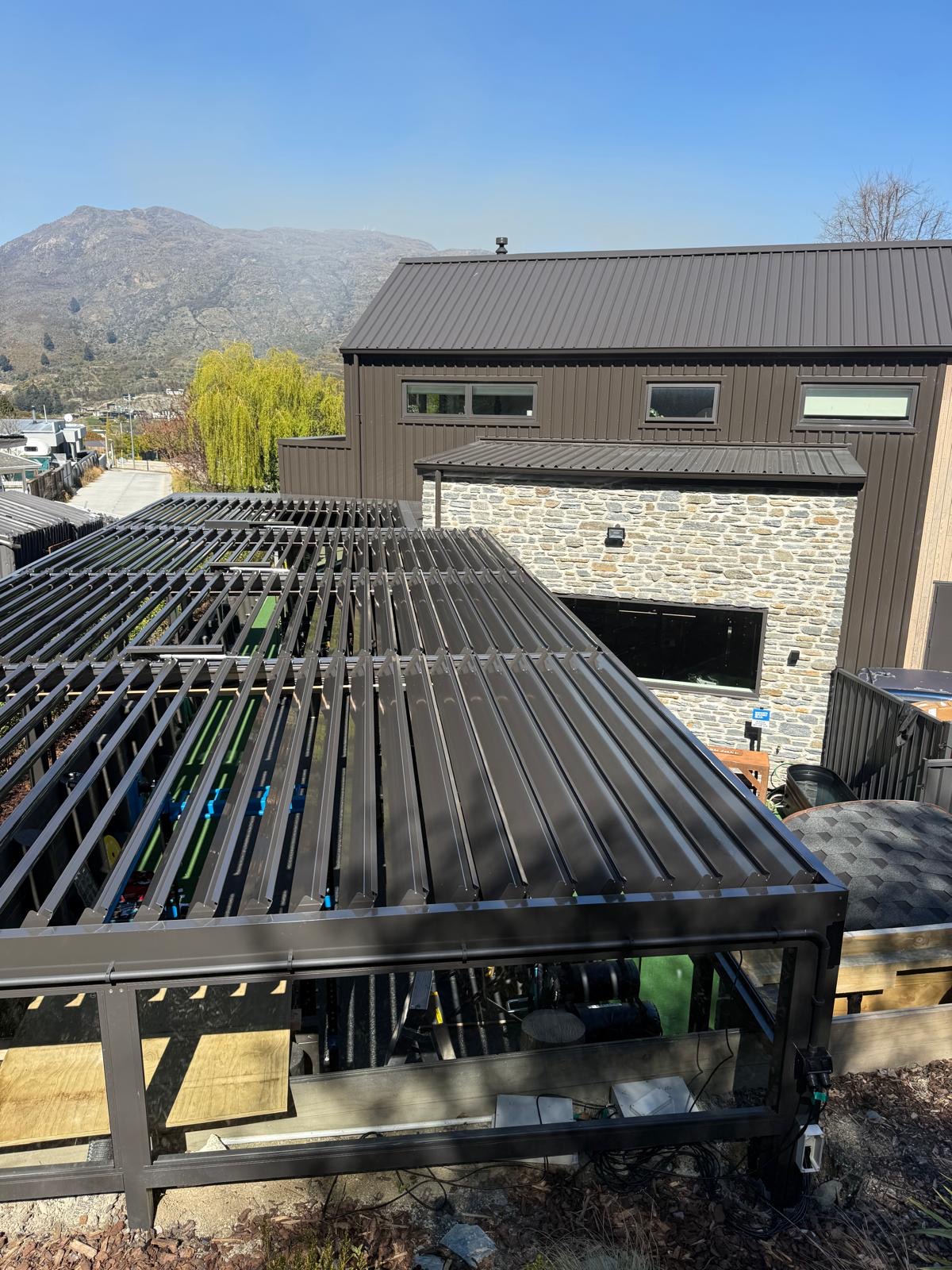 Bronze louvre roof seen from above beside a stone-clad home in Queenstown