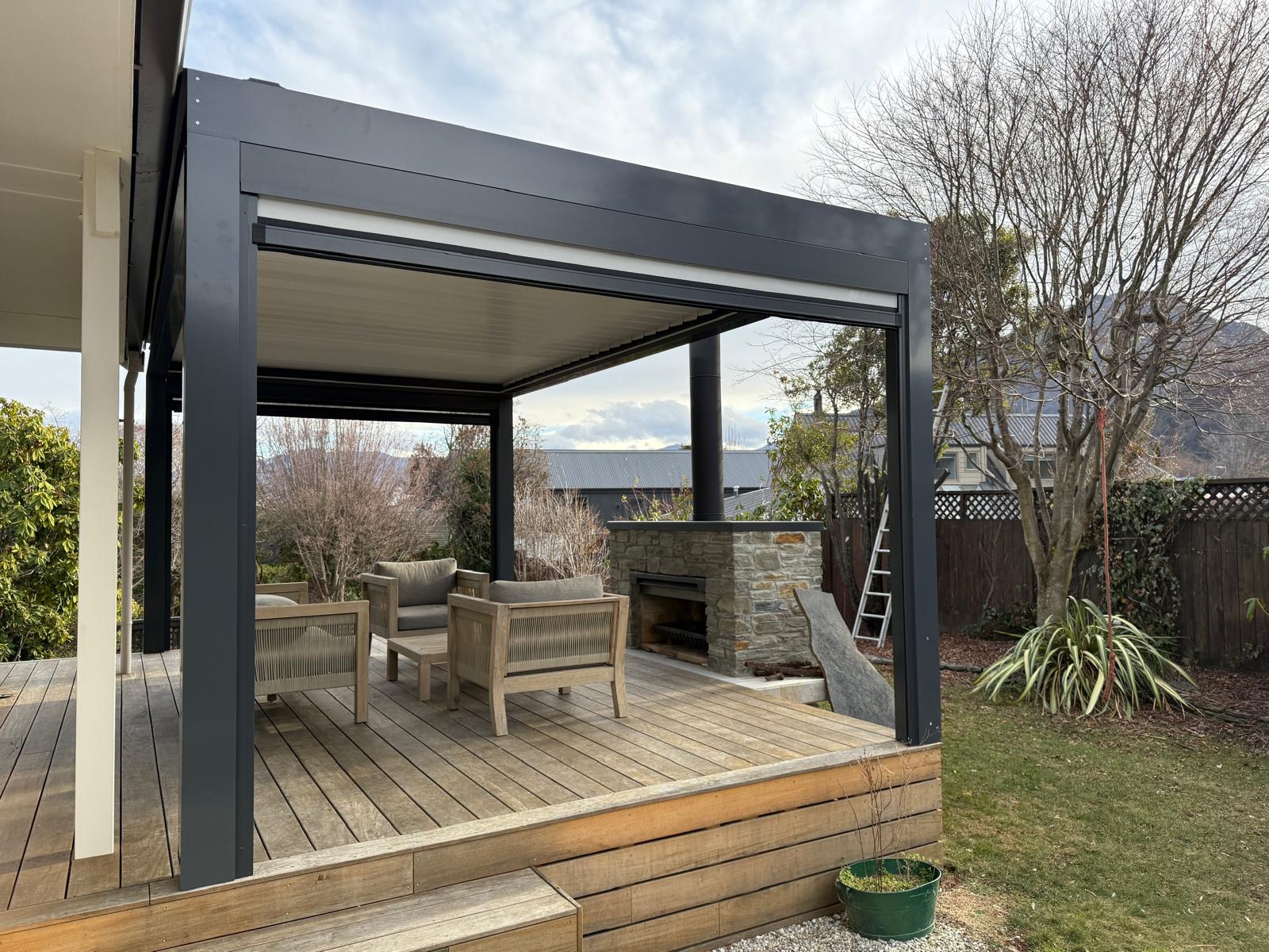 Grey louvre roof over a timber deck and stone fireplace in Queenstown